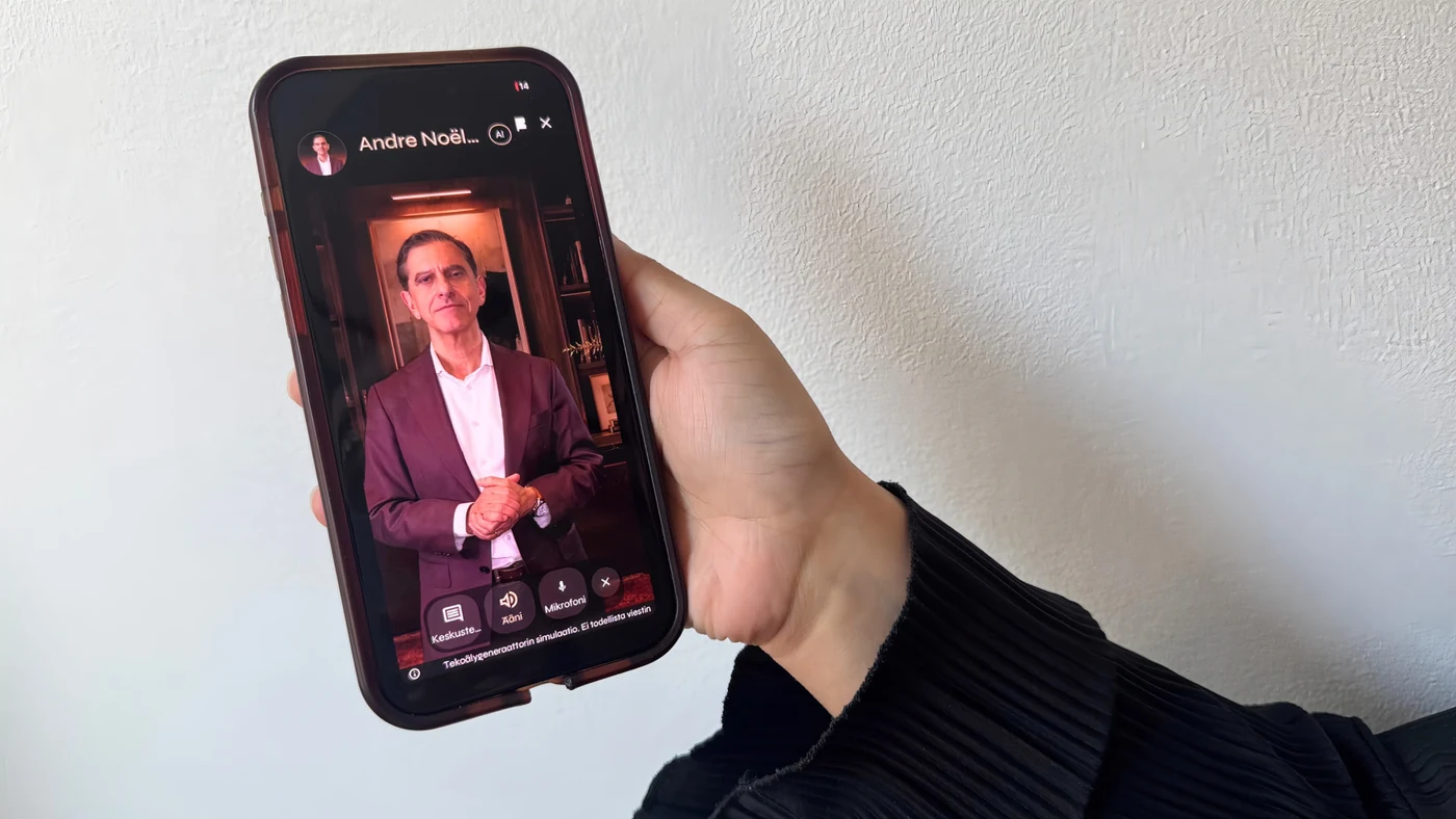 A person holding a phone with a video conversation open with André Noël Chaker's official Persona AI avatar